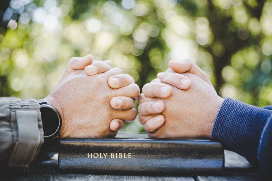 Hands of People Praying on Top of a Bible